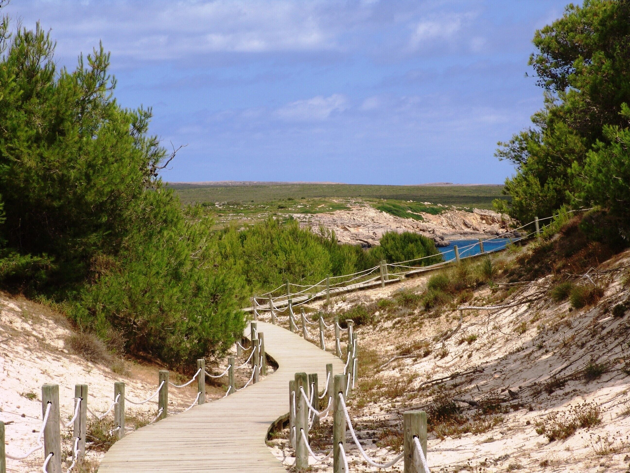 A wooden boardwalk leading to a beach with a clear view of the sea and rocky landscape.