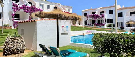 A poolside area with lounge chairs, a thatched umbrella, and a signboard.