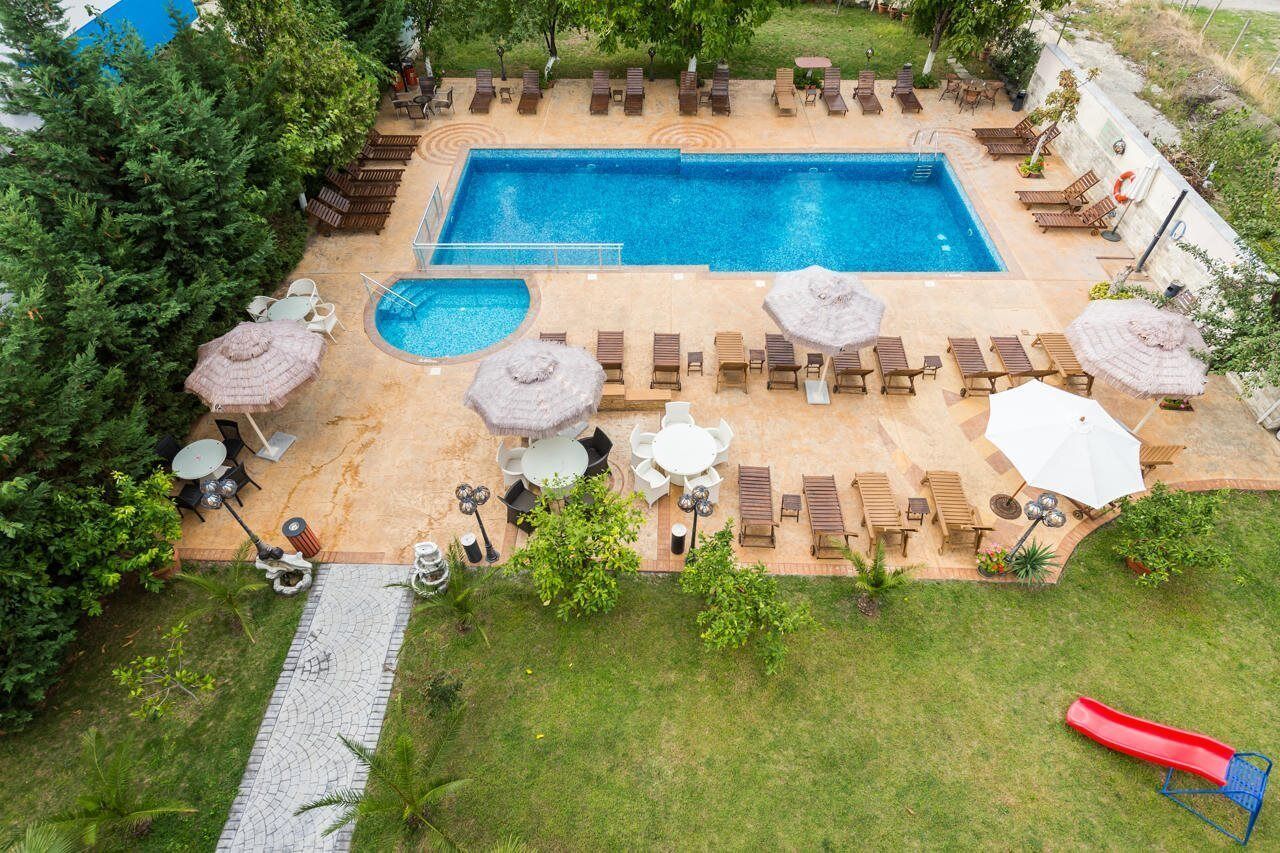 A rectangular pool with lounge chairs and umbrellas, surrounded by greenery and a small slide.