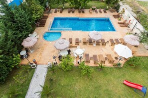 Una piscina rettangolare con lettini e ombrelloni, immersa nel verde e con una piccola scivolata.