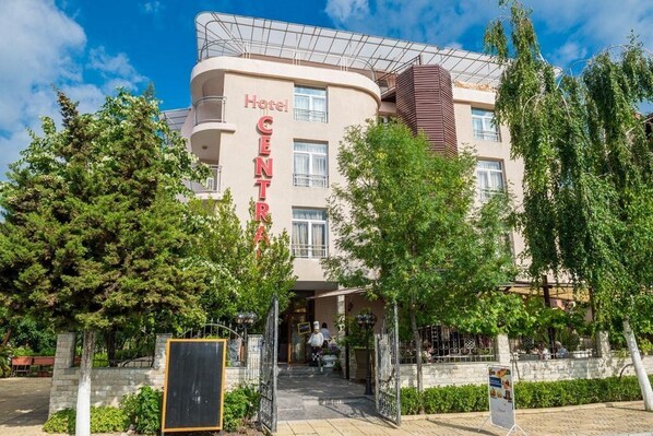 Un hôtel à la façade incurvée, avec une enseigne bien visible indiquant «Hôtel CENTER», et une entrée fermée par un portail, un chemin menant au bâtiment.