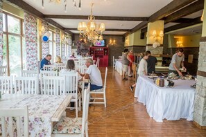 Un ristorante con tavoli e sedie di legno bianco, un lampadario e un televisore sullo sfondo.
