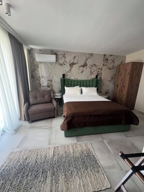 Una camera da letto con un letto imbottito verde, una coperta marrone, una poltrona marrone, un tavolino rotondo e un'armadio in legno.