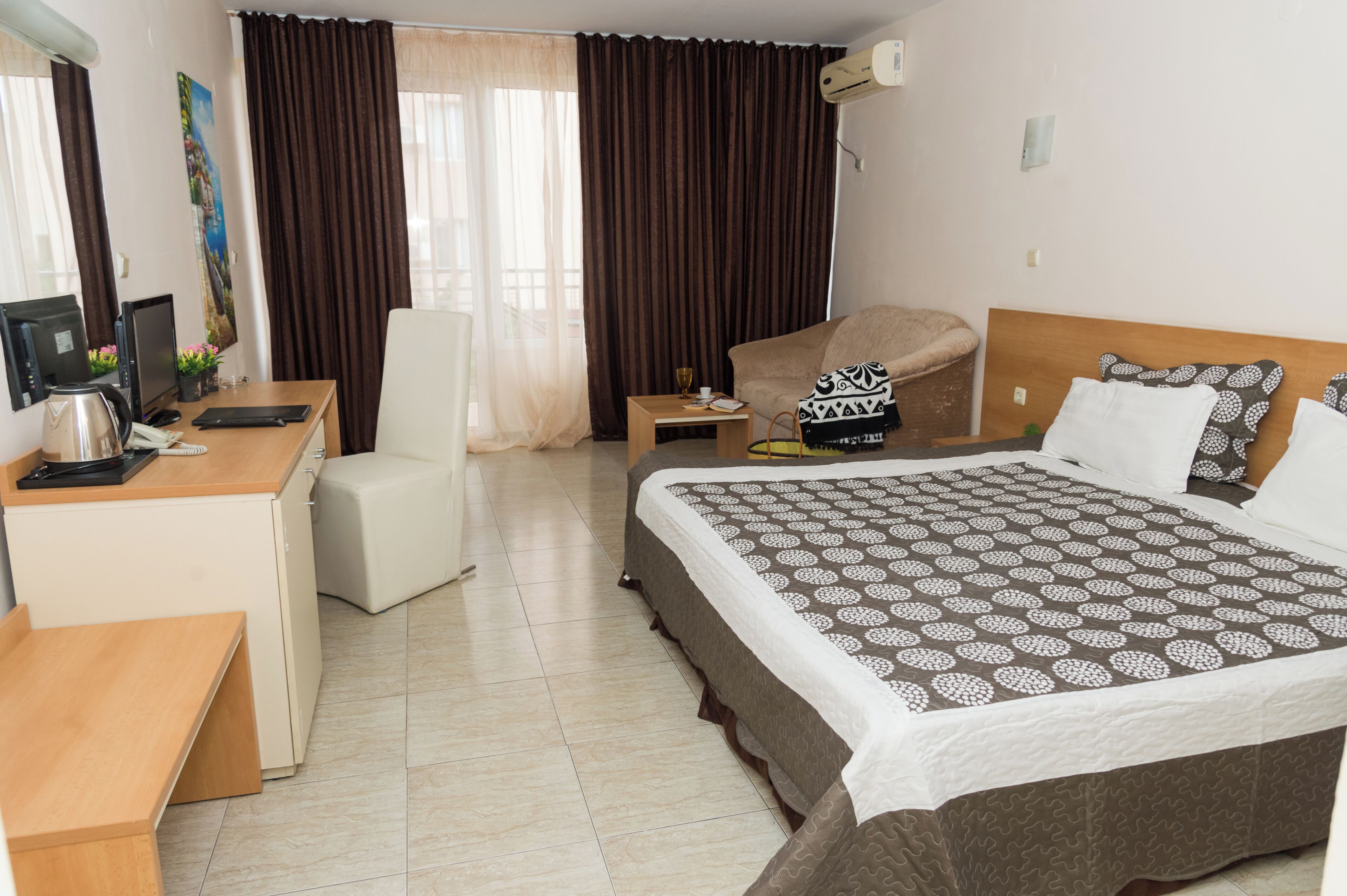 A hotel room with a bed, a desk, a chair, a coffee maker, and a window with curtains.