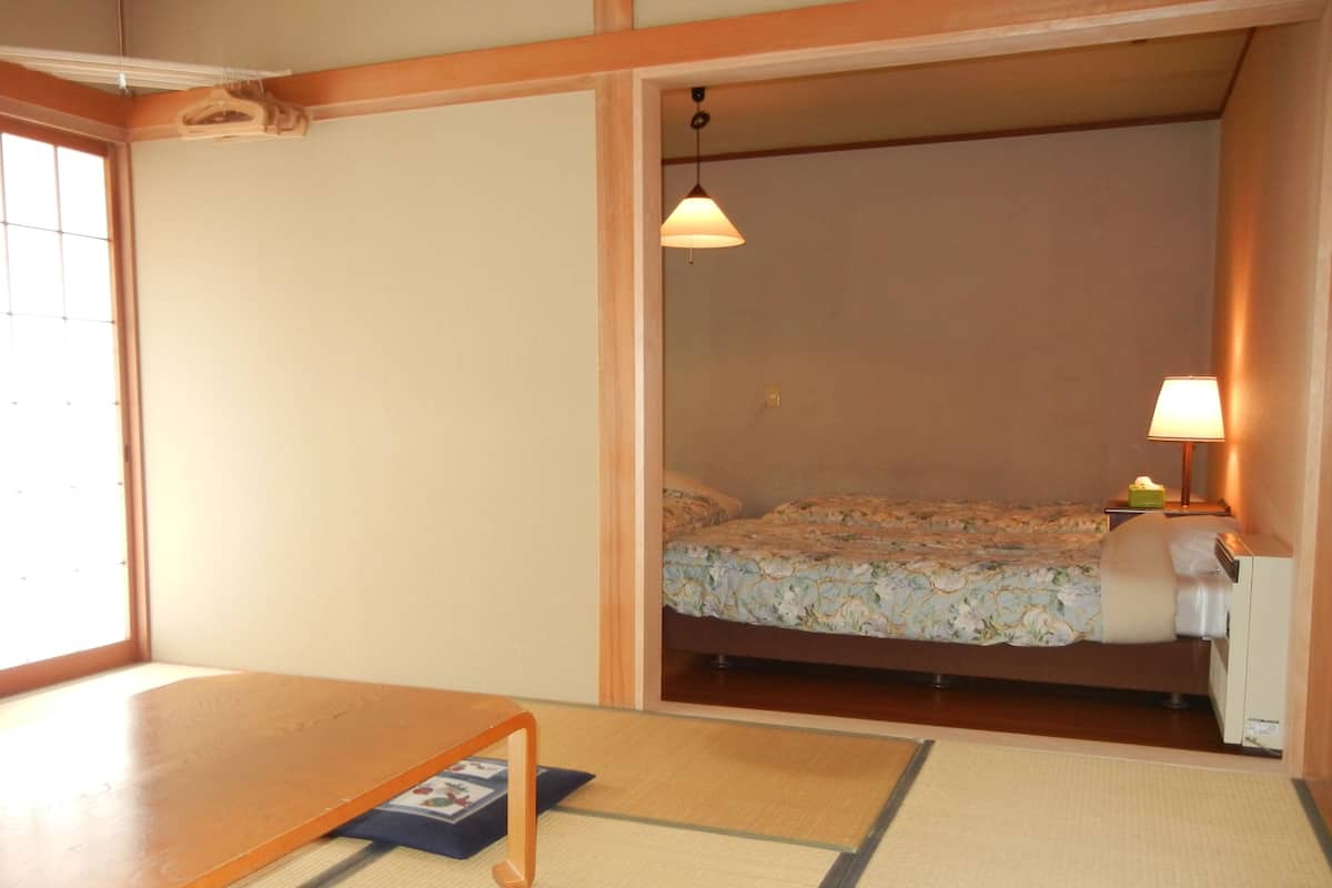 Une pièce avec un lit, une table, une lampe et une fenêtre.