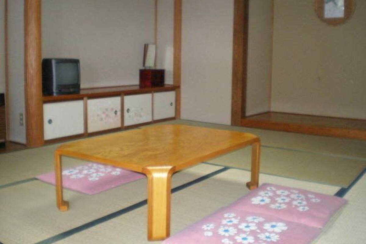 Une pièce avec des tatamis, une table en bois, un téléviseur et un meuble.