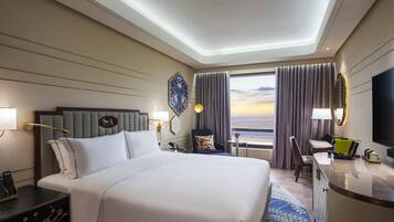 A hotel room with a bed, bedside table, desk, chair, and a large window with curtains.
