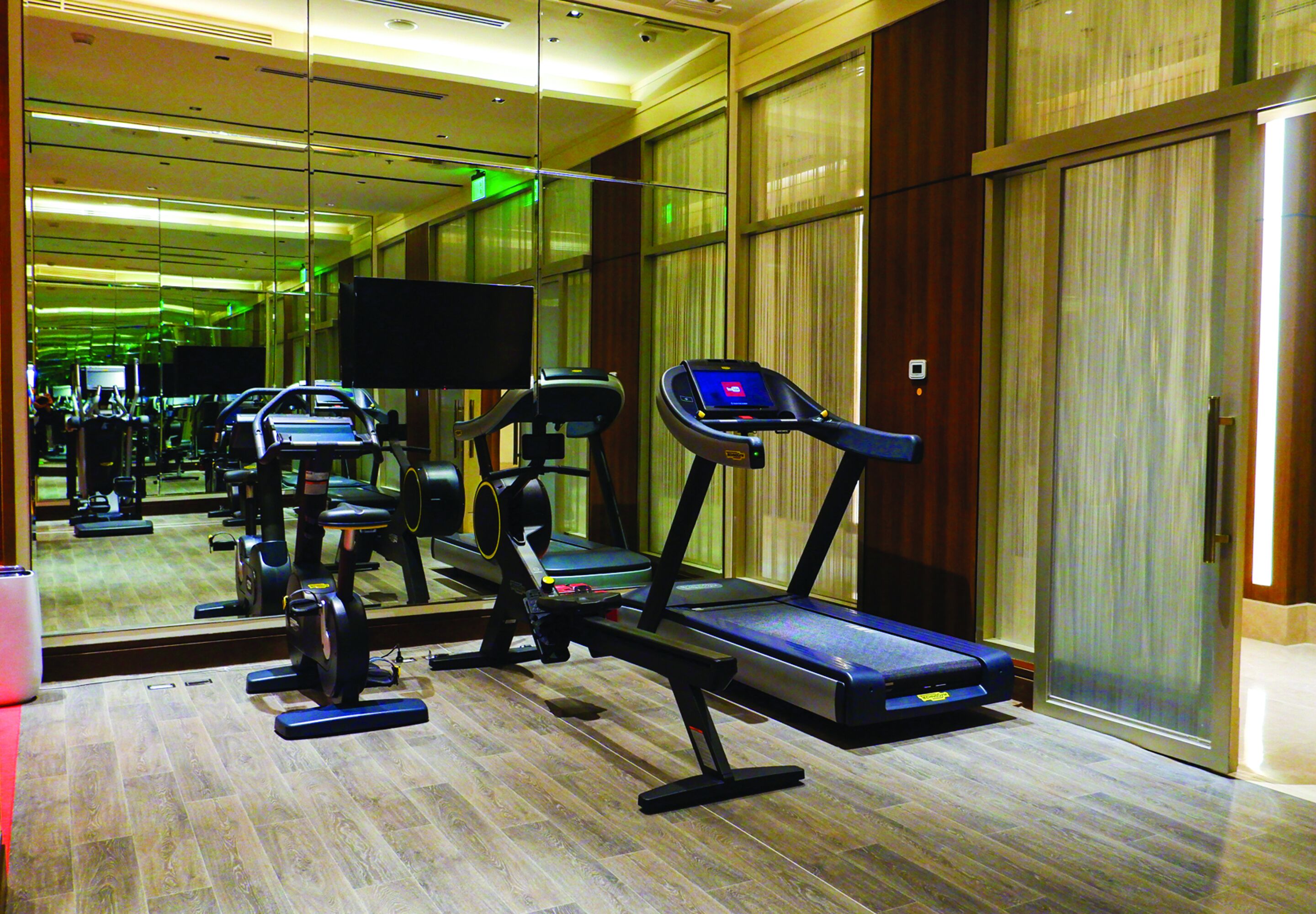 A gym with treadmills, exercise bikes, and a mirrored wall.