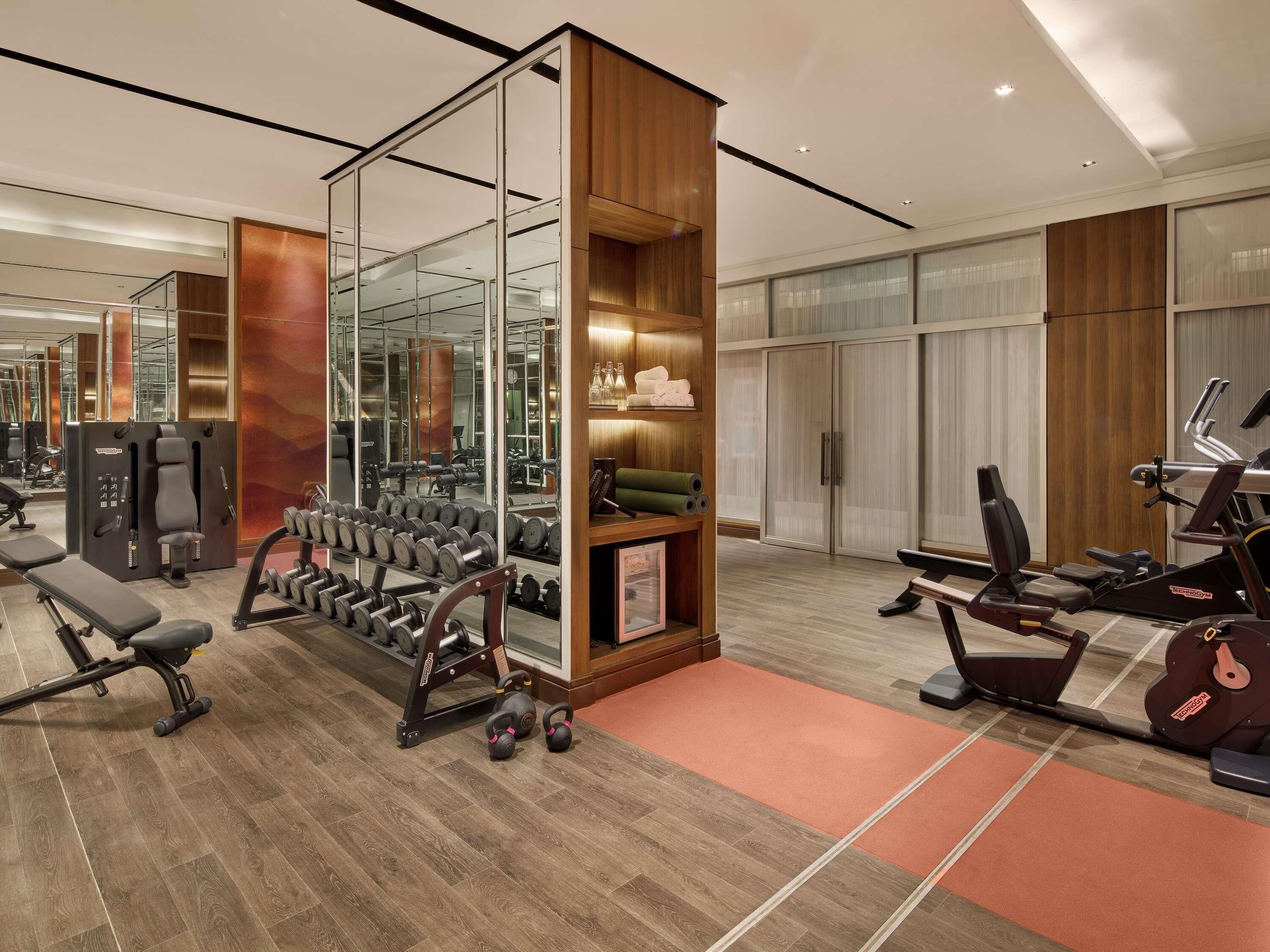Une salle de sport moderne équipée de divers appareils d’exercice, notamment des haltères, un banc et des appareils de cardio.