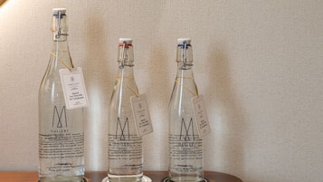 Tres botellas de vidrio con la etiqueta 'Gallery Hotel Collection' y etiquetas, sobre una superficie de madera frente a una pared texturizada.