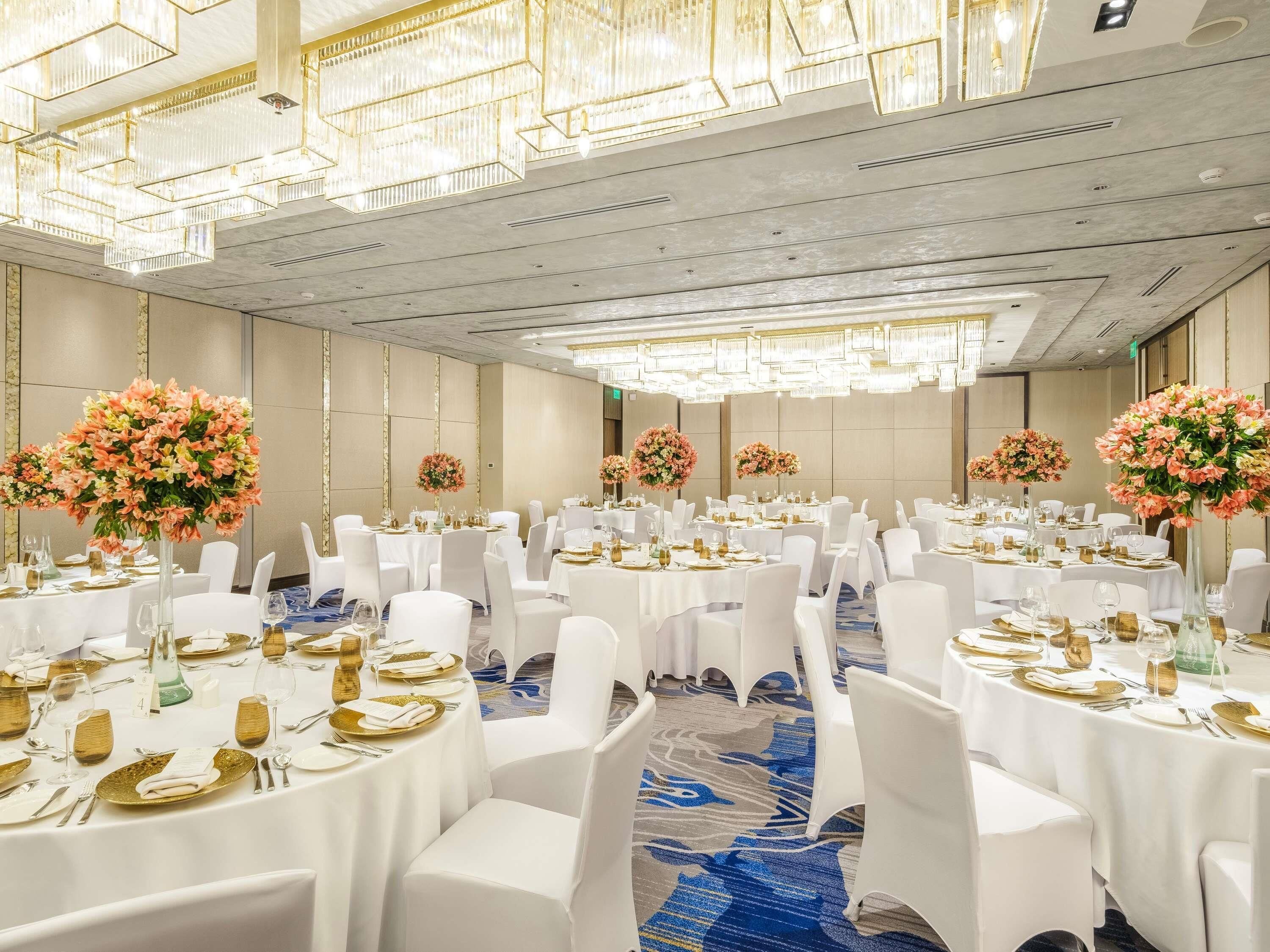 Une salle de banquet avec des tables rondes, des chaises blanches et des centres de table floraux.
