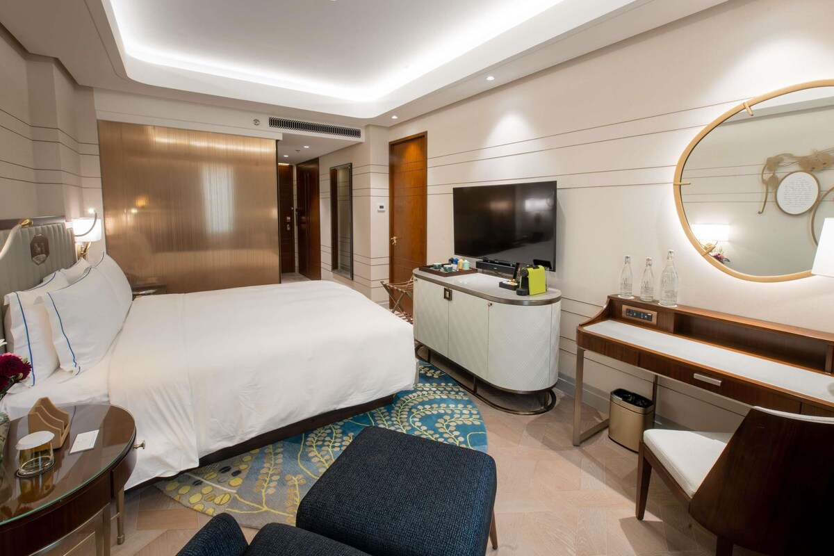 A modern hotel room with a large bed, a desk, a TV, and a mirror.