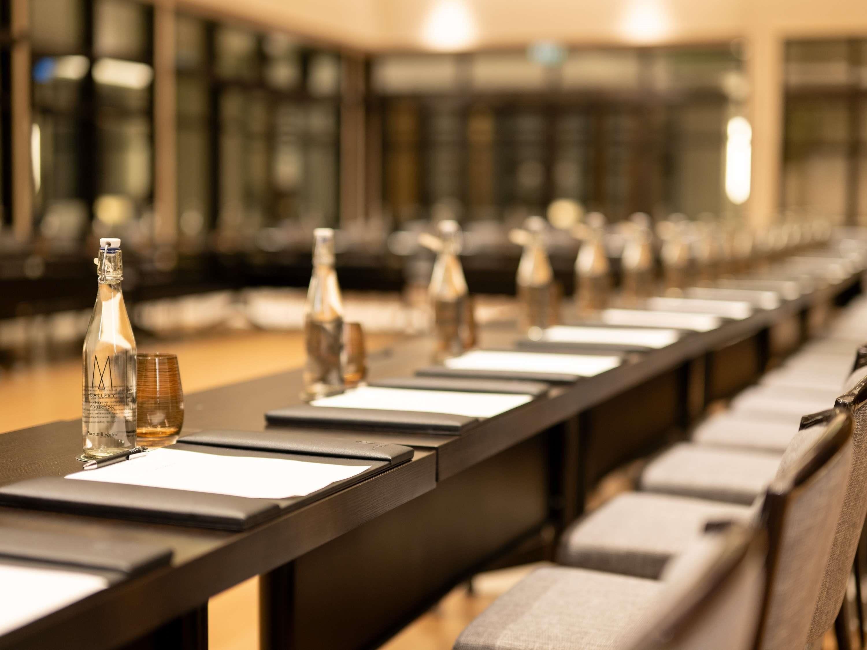 Un salón de conferencias con mesas, sillas y botellas de agua dispuestas en filas.