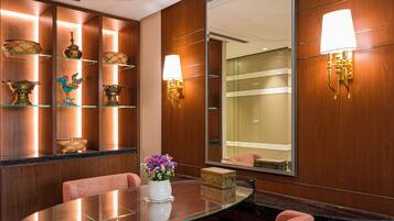 A hotel lobby with a glass table, red upholstered chairs, decorative items on shelves, and a large mirror.