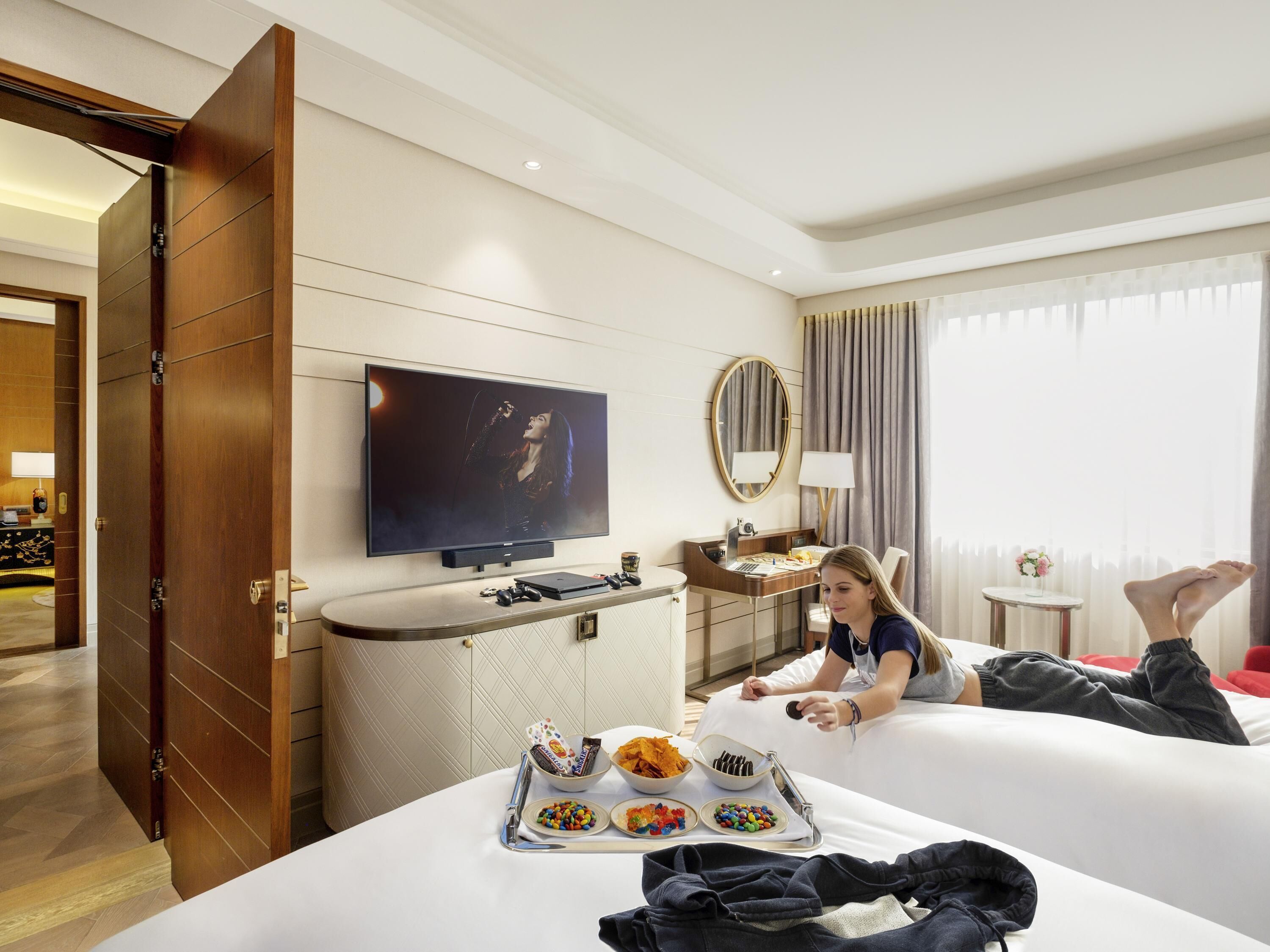 A hotel room with a bed, a TV, a desk, and a window with curtains.