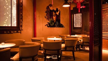 Interior de un restaurante tenuemente iluminado con decoración tradicional, incluyendo mobiliario de madera y faroles rojos.