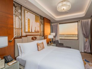 Une chambre d’hôtel avec un grand lit, un bureau avec un téléphone, une chaise, une lampe de bureau, une fenêtre avec des rideaux et des œuvres d’art accrochées au mur.