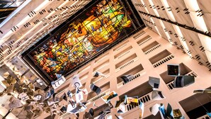 Un atrio moderno con un amplio ventanal de vitral, varios balcones e lámparas colgantes.