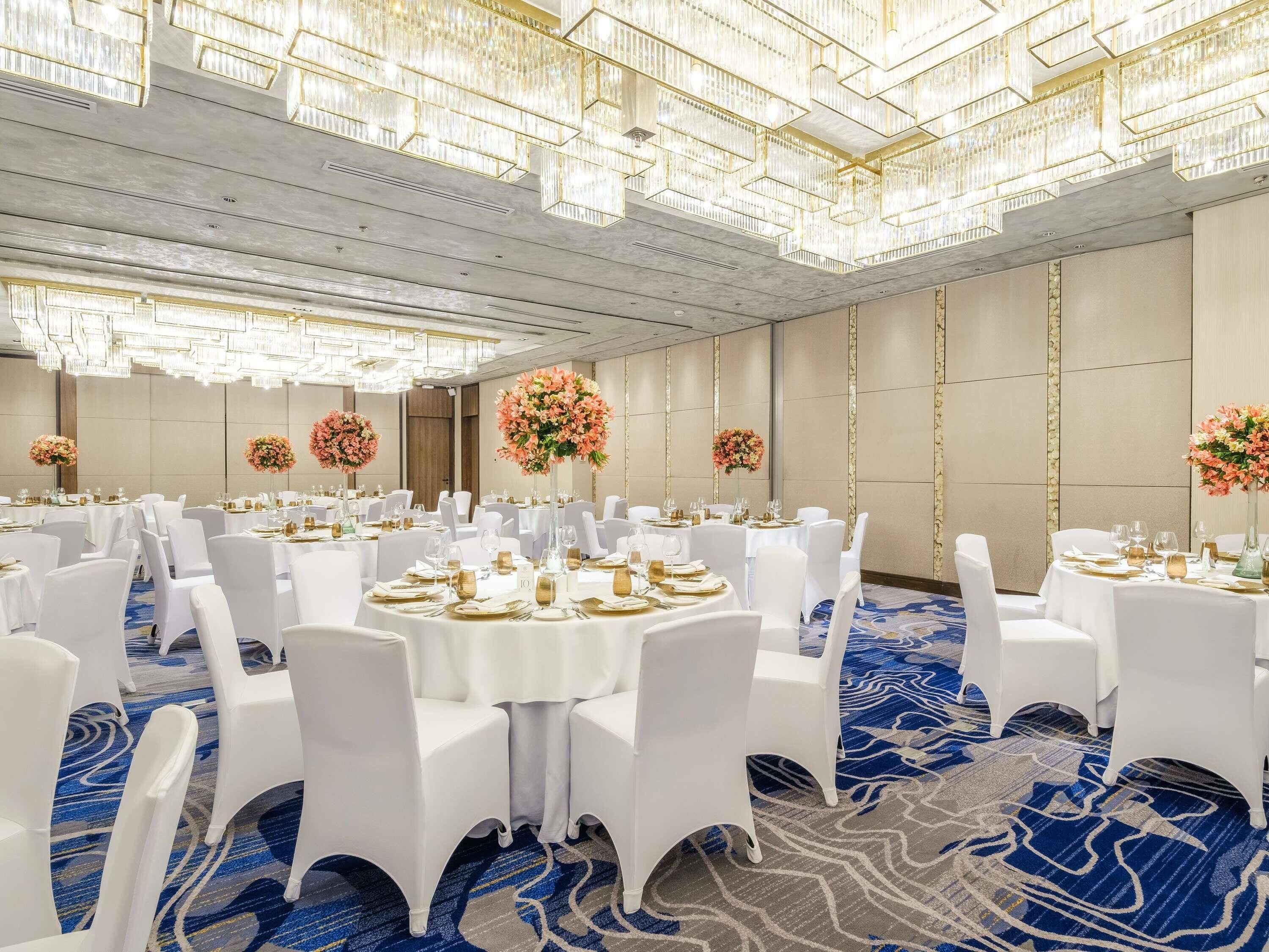 A banquet hall with round tables, white chairs, and floral centerpieces.
