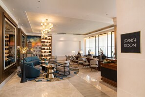 Een ruime lobby met een blauwe bank, een kroonluchter, een receptiebalie en een boekenkast.