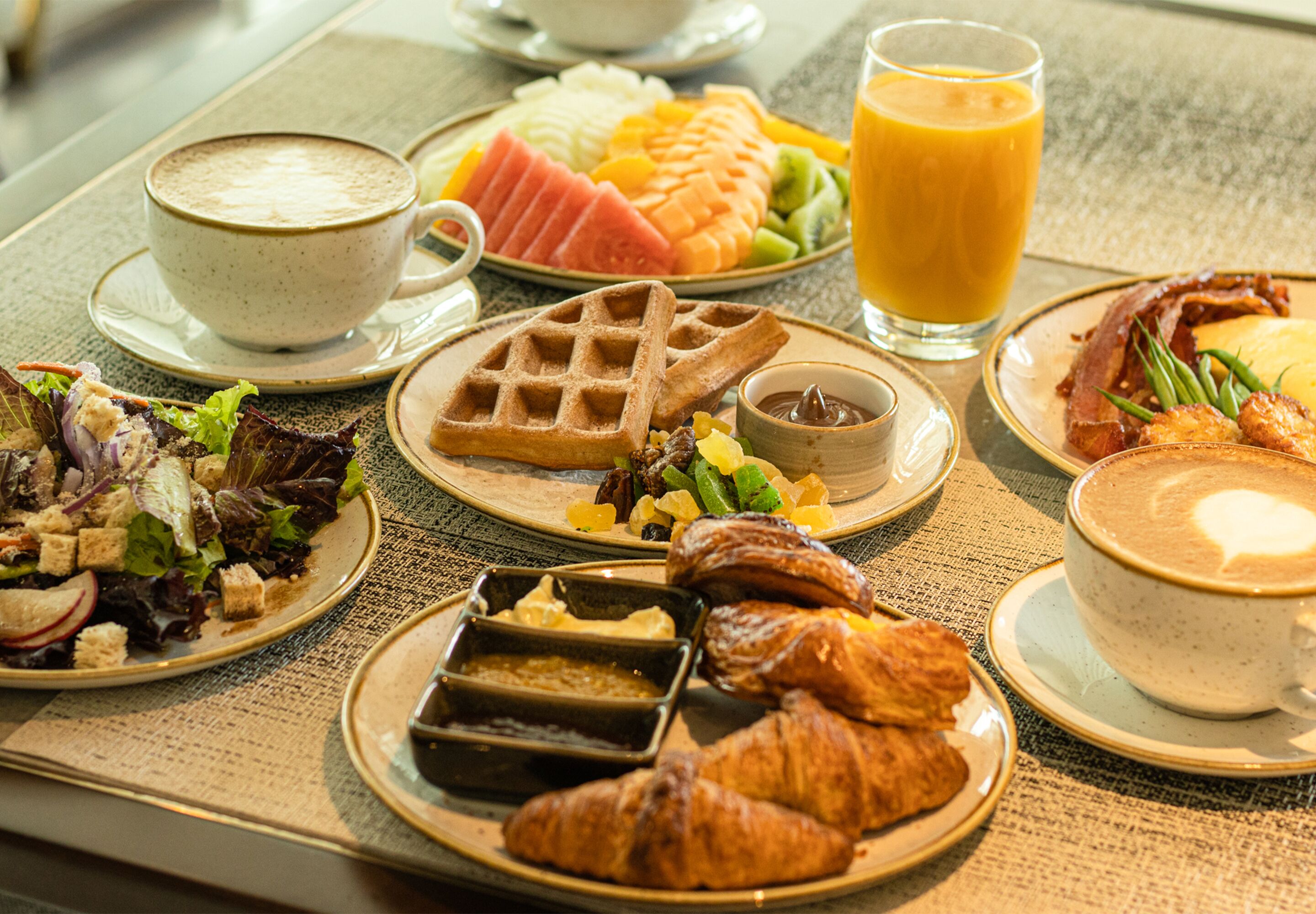 A breakfast spread with waffles, croissants, and various fruits on a table.