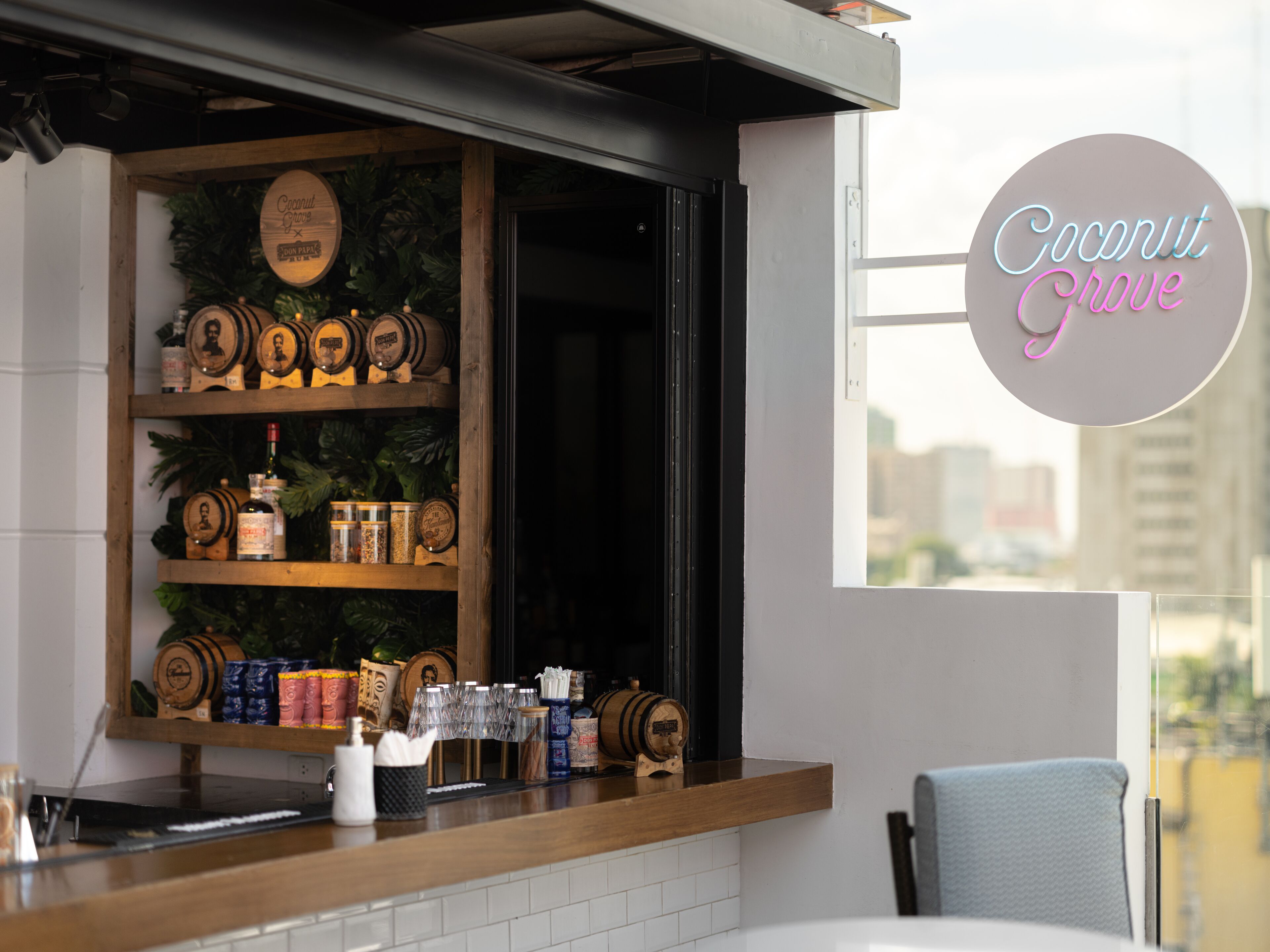 Een bar met houten planken waarop flessen en glazen staan, een neonbord met de tekst 
