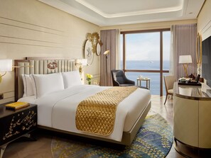 A hotel room with a large bed, a desk, a chair, and a view of the sea. - Admiral Hotel Manila - MGallery Collection (Manila)