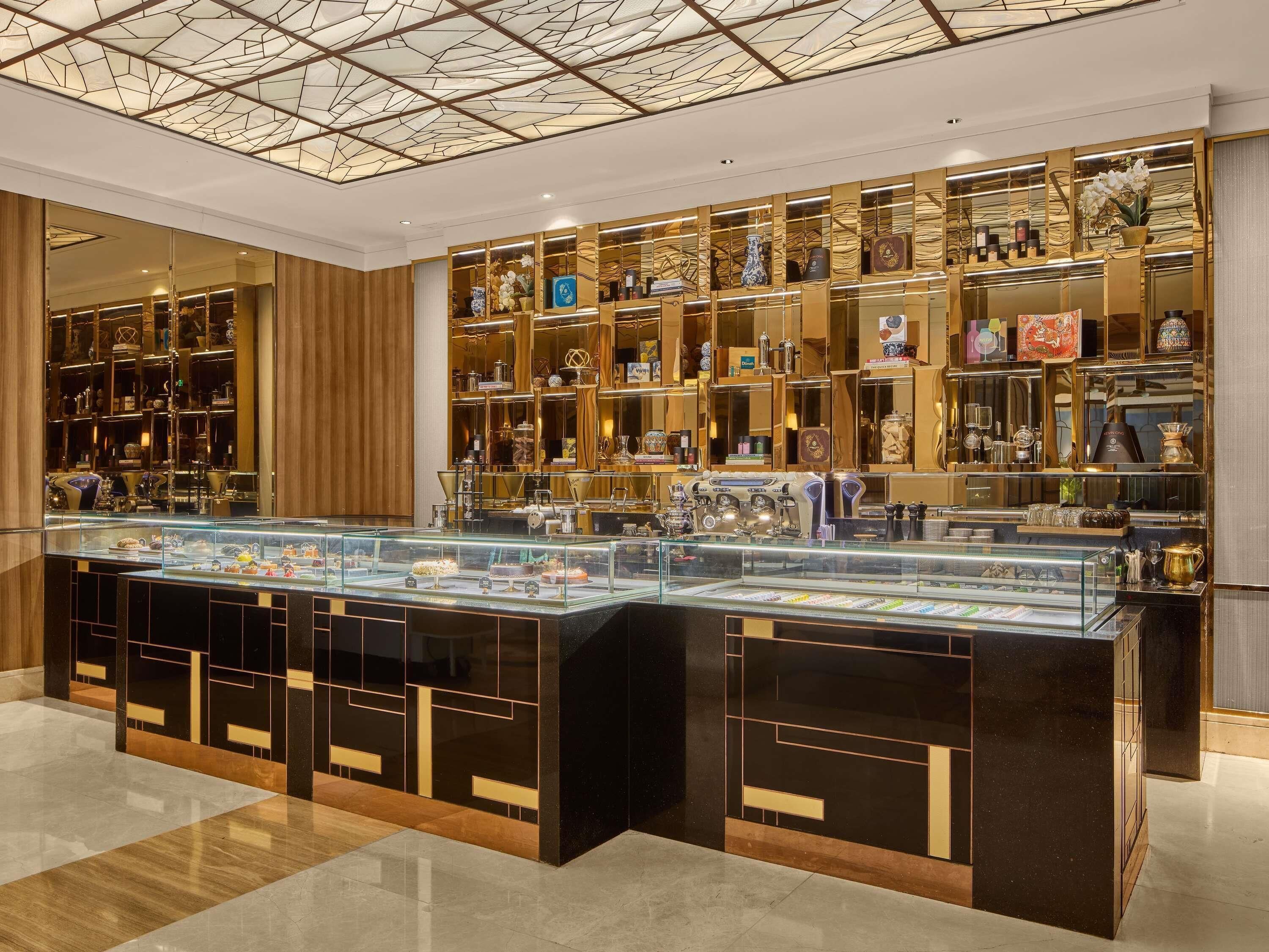 Lobby di un hotel di lusso con una vetrina centrale, pannelli in legno e un soffitto a motivi geometrici.