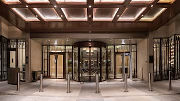 L’entrée d’un hôtel, avec une porte tournante, une barrière en verre et un plafond décoratif.