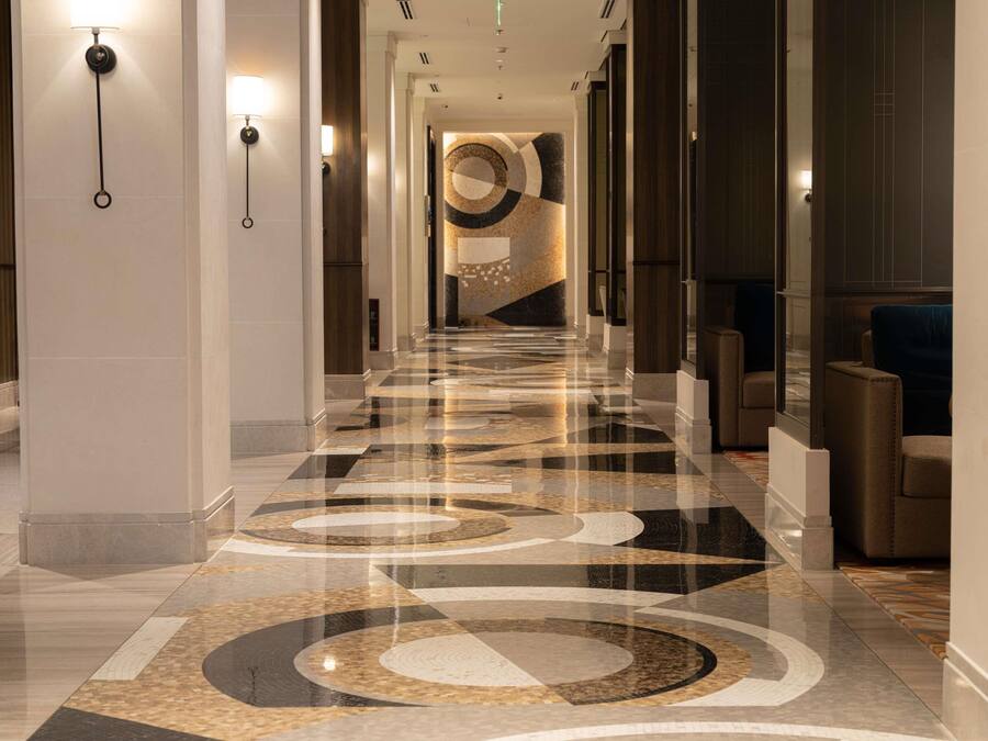 A long, polished hallway with a patterned floor, columns, and wall sconces.