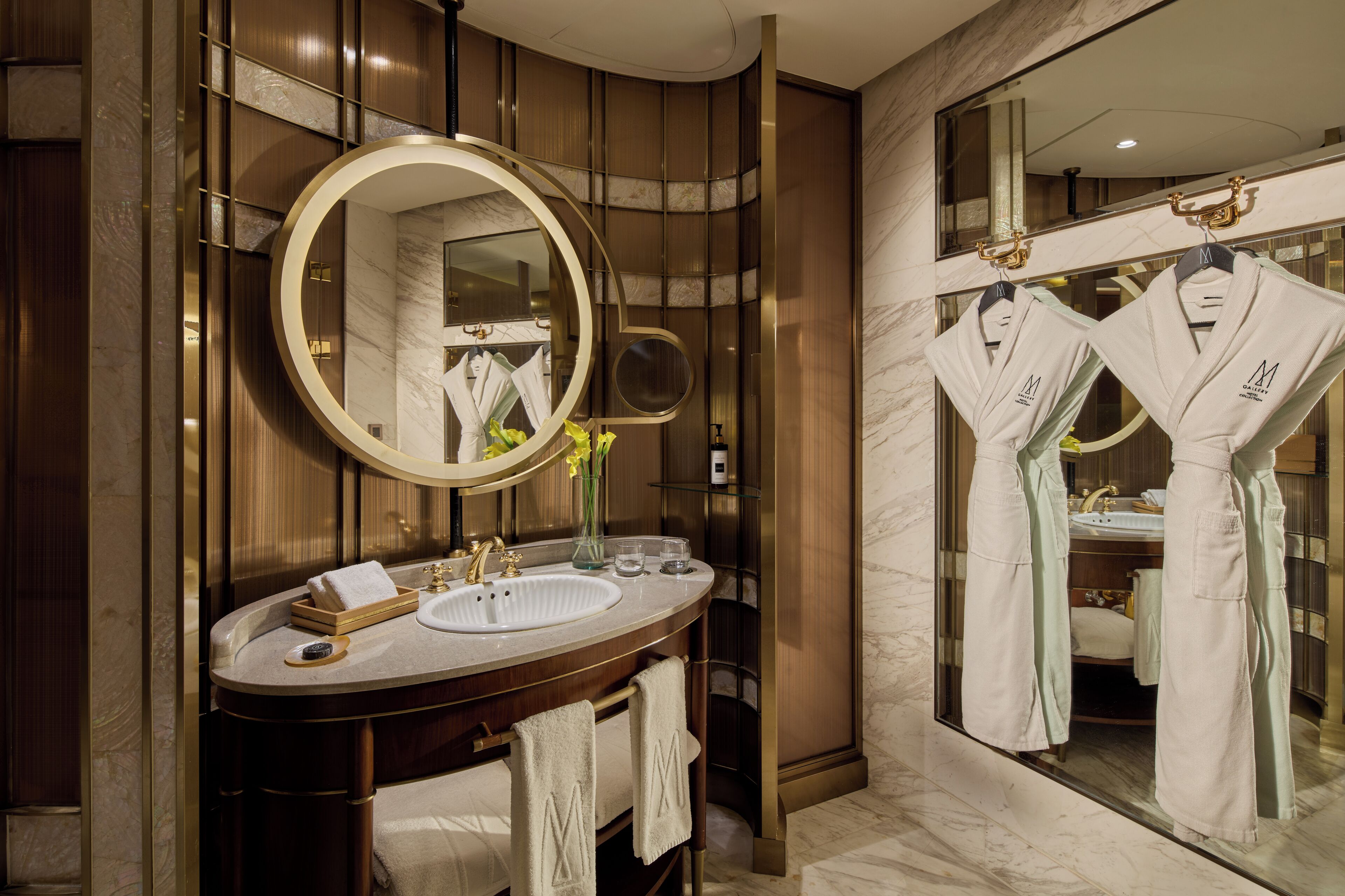 A modern bathroom with a large mirror, a vanity with a sink, and two robes hanging on hooks.