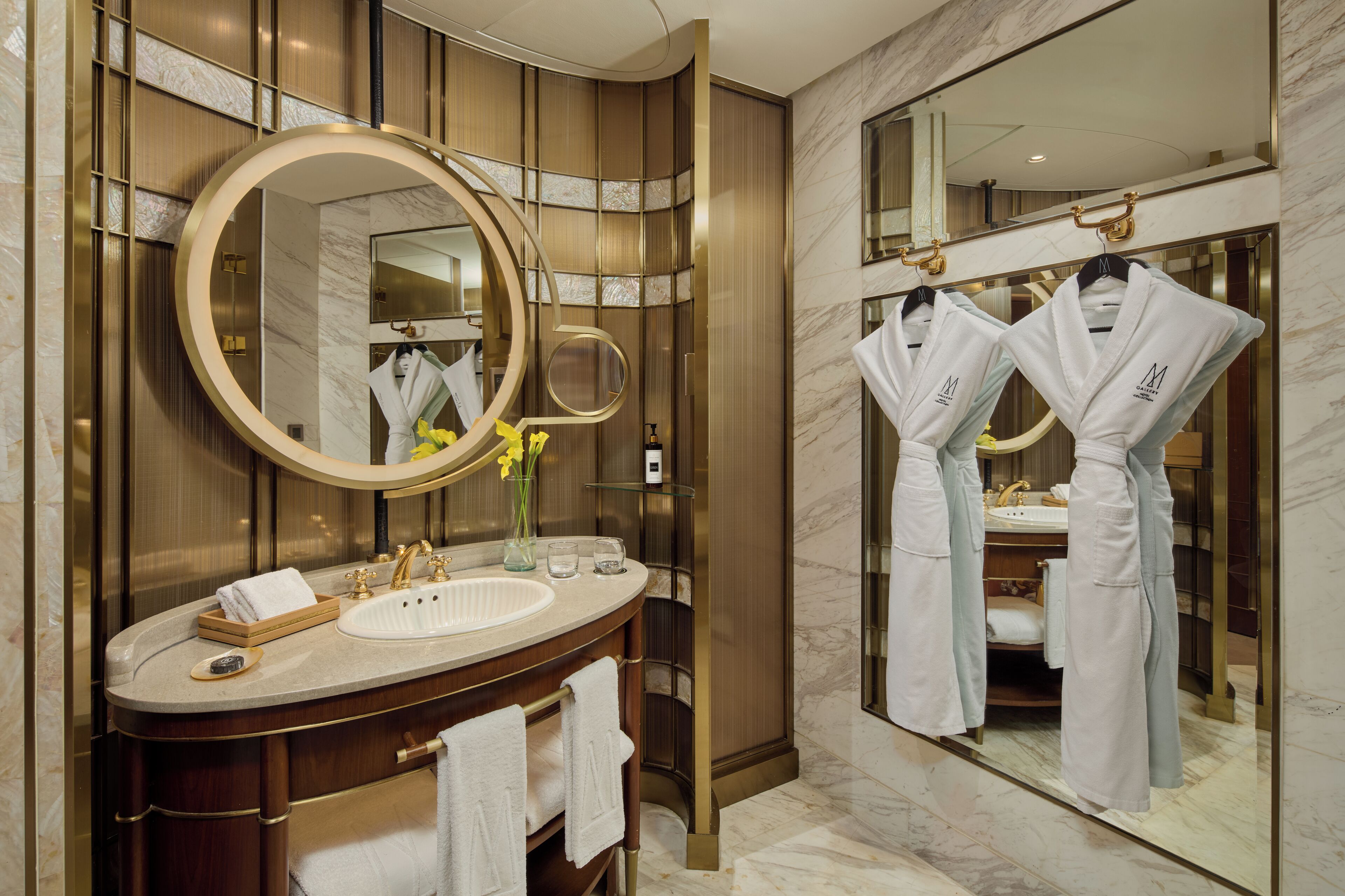 A modern bathroom with a large mirror, a vanity with a sink, and two robes hanging on hooks.