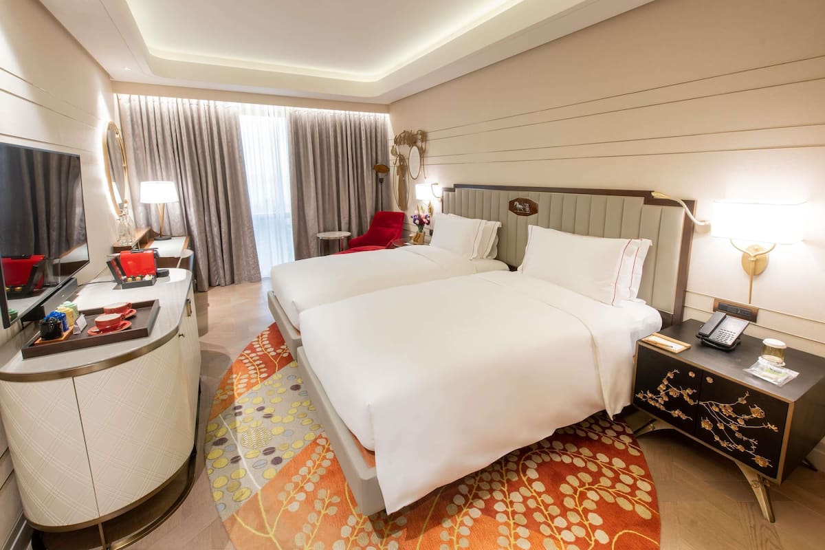 A hotel room with a bed, a desk, a chair, a TV, and a phone.