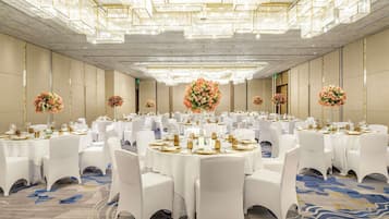 Un salón de banquetes con mesas redondas, sillas blancas y centros de mesa florales.