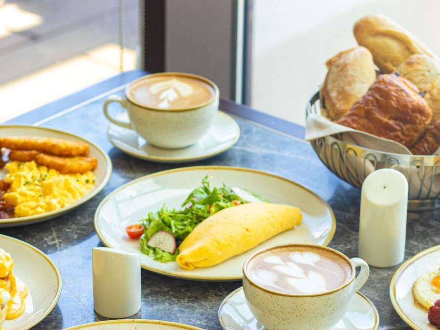 A breakfast table with plates of food, a cup of coffee, and a basket of bread.