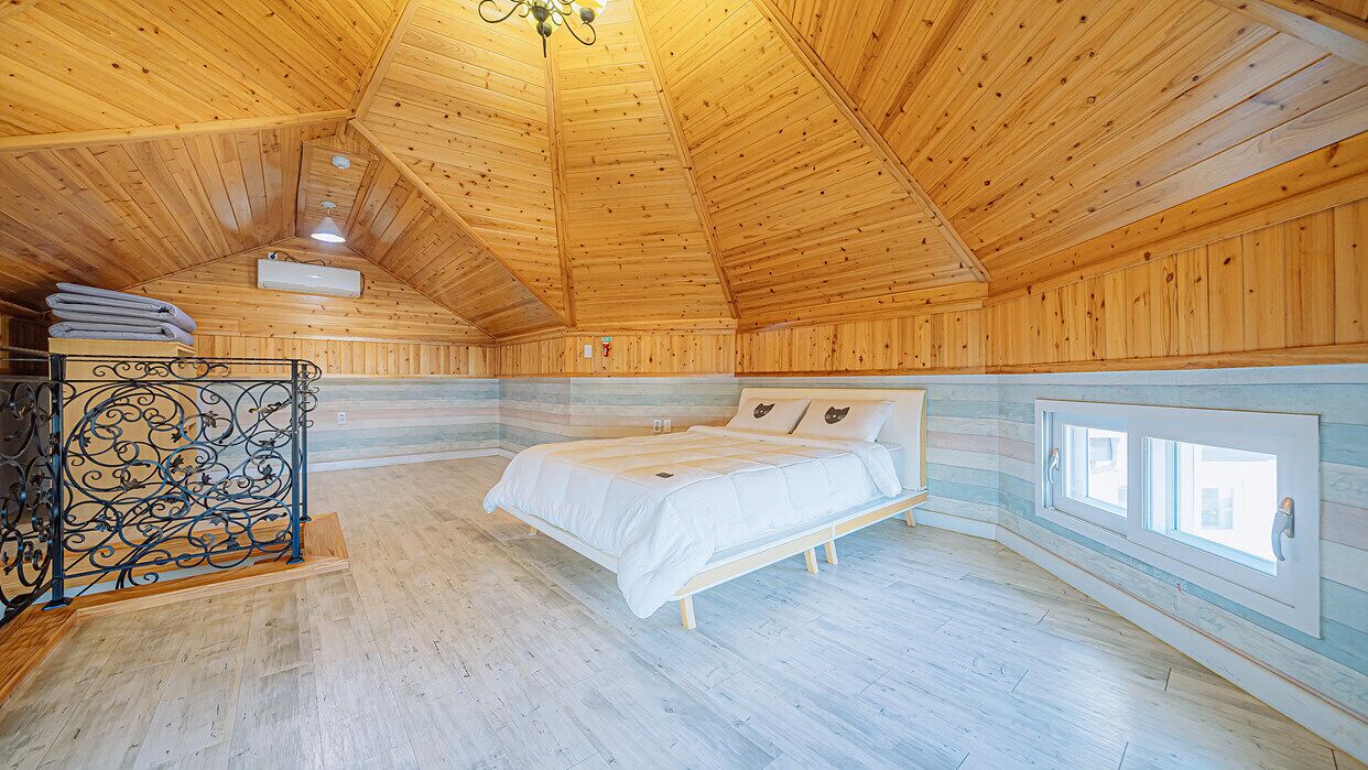 A wooden cabin interior with a bed, a metal railing, and a window.