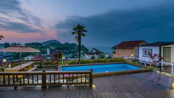 Una terraza de madera con piscina, rodeada de casas y vistas al mar.