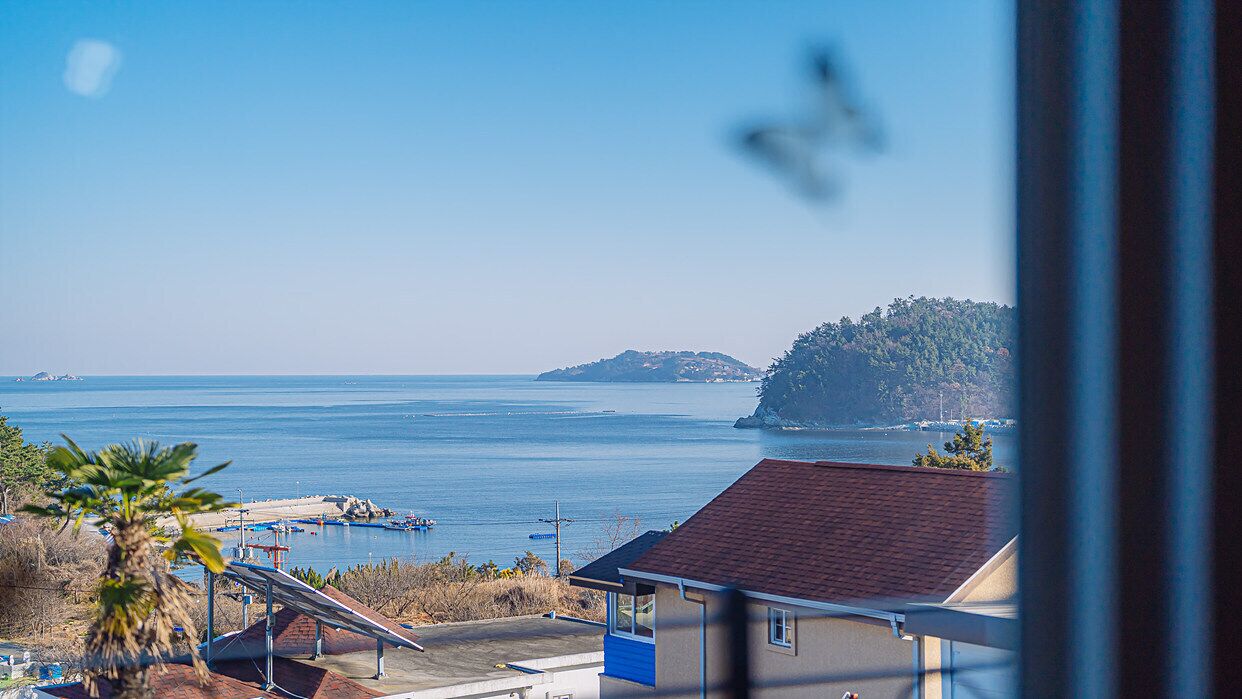 Blick auf die Küste, strahlend blauer Himmel, eine vorgelagerte Insel und ein kleines Gebäude mit rotem Dach.