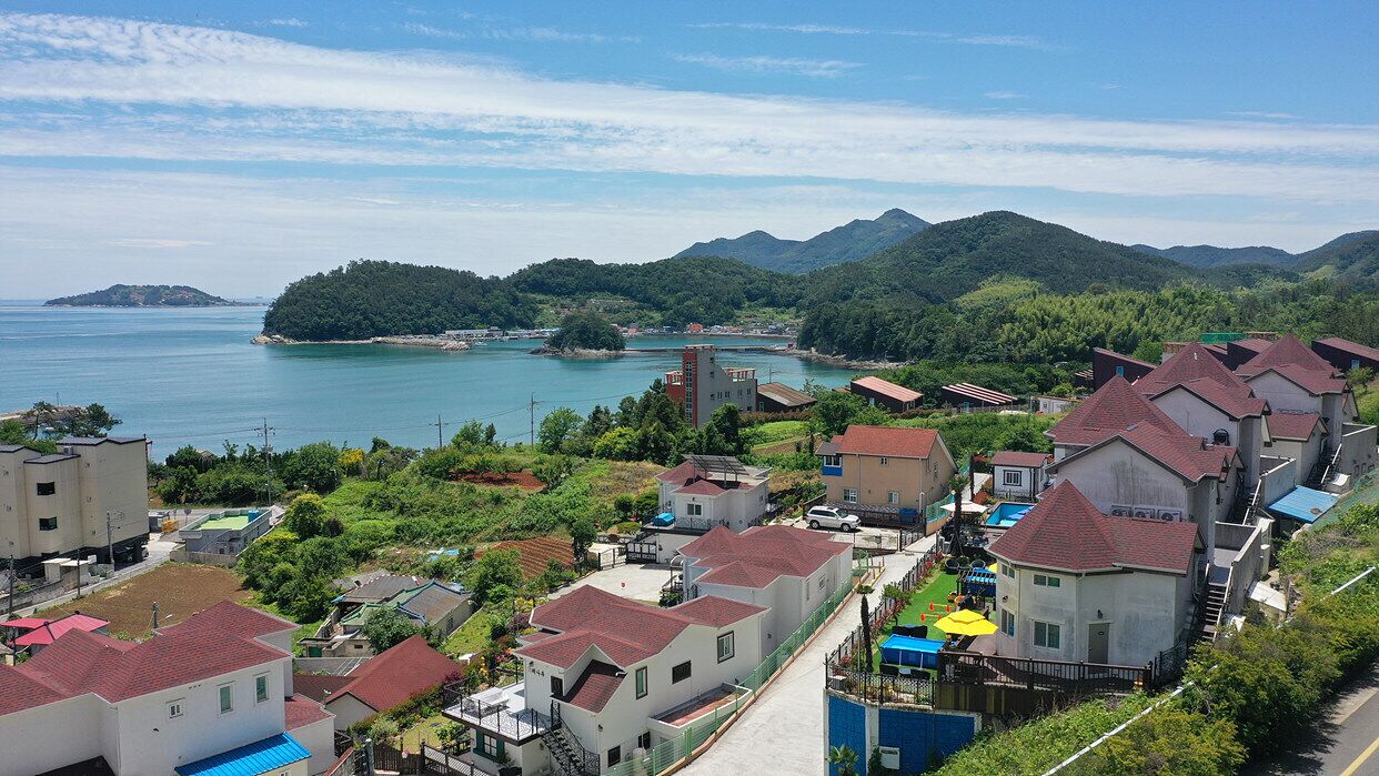 A coastal residential area with houses, a small church, and a view of the sea and mountains.