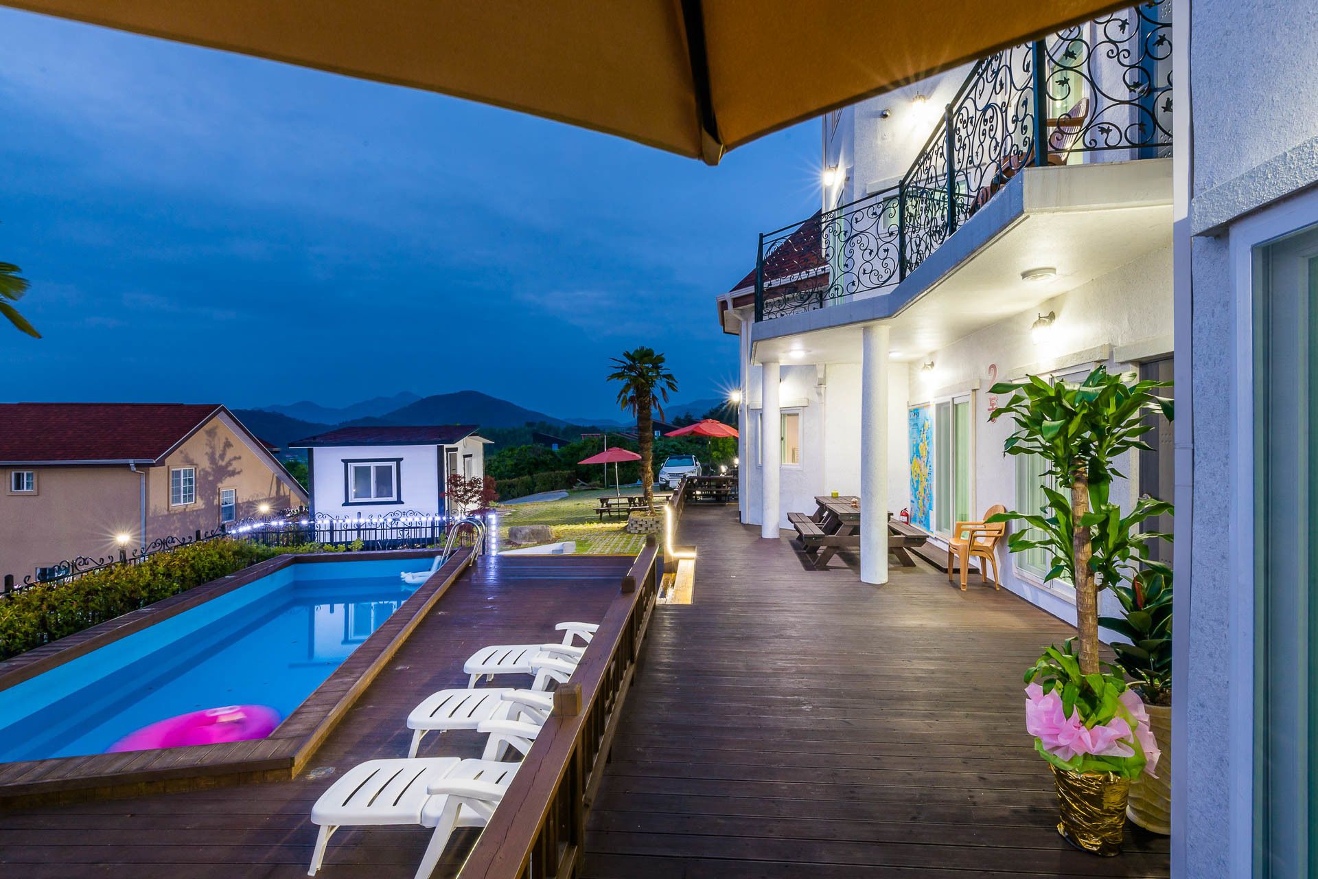 A poolside area with lounge chairs, a wooden deck, and a building with a balcony.
