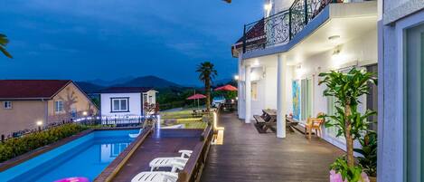 A poolside area with lounge chairs, a wooden deck, and a building with a balcony.