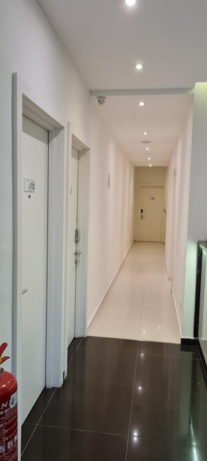 Un pasillo con puertas a ambos lados, un extintor a la izquierda y suelo de baldosas.