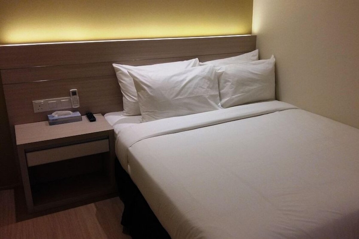 A hotel room with a bed, bedside table, and a wall-mounted power outlet.