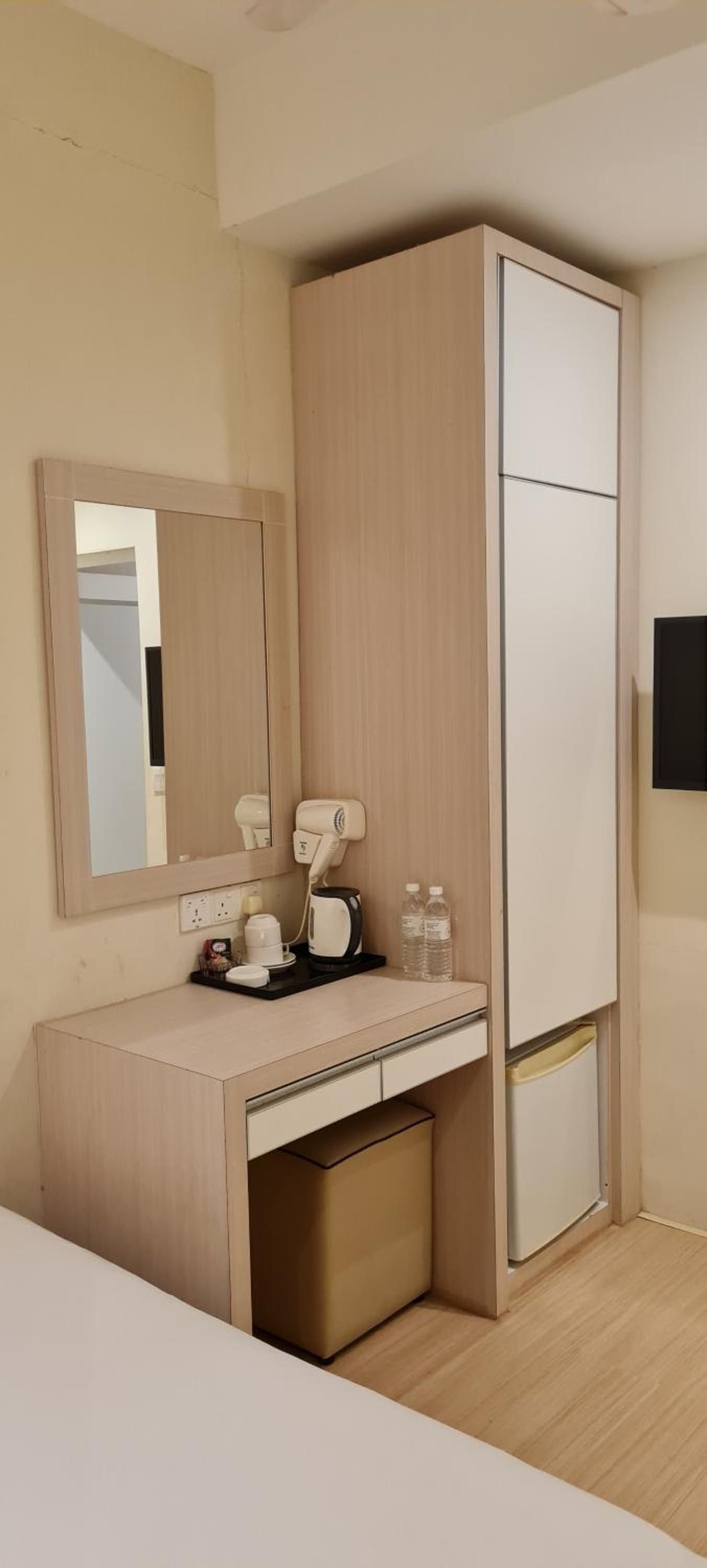 A compact hotel room with a built-in desk, a hairdryer, a kettle, and a mirror.