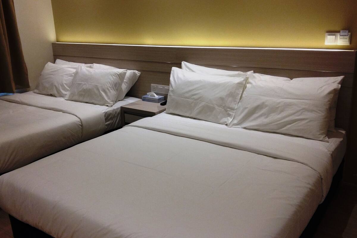 A hotel room with two beds, each with white linens, a nightstand with a lamp, and a wall-mounted light.
