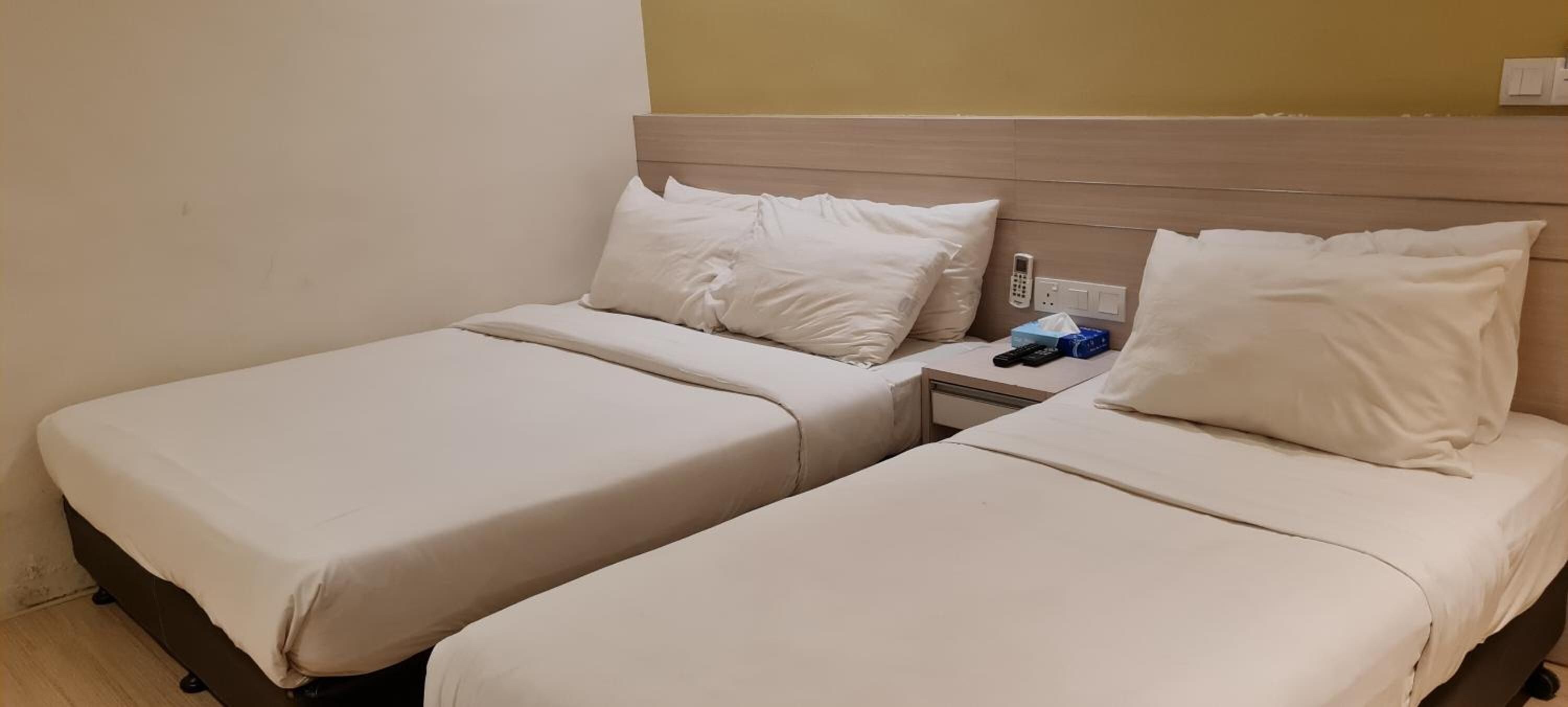 A hotel room with two beds, a bedside table with a phone and a tissue box, and a wall socket.