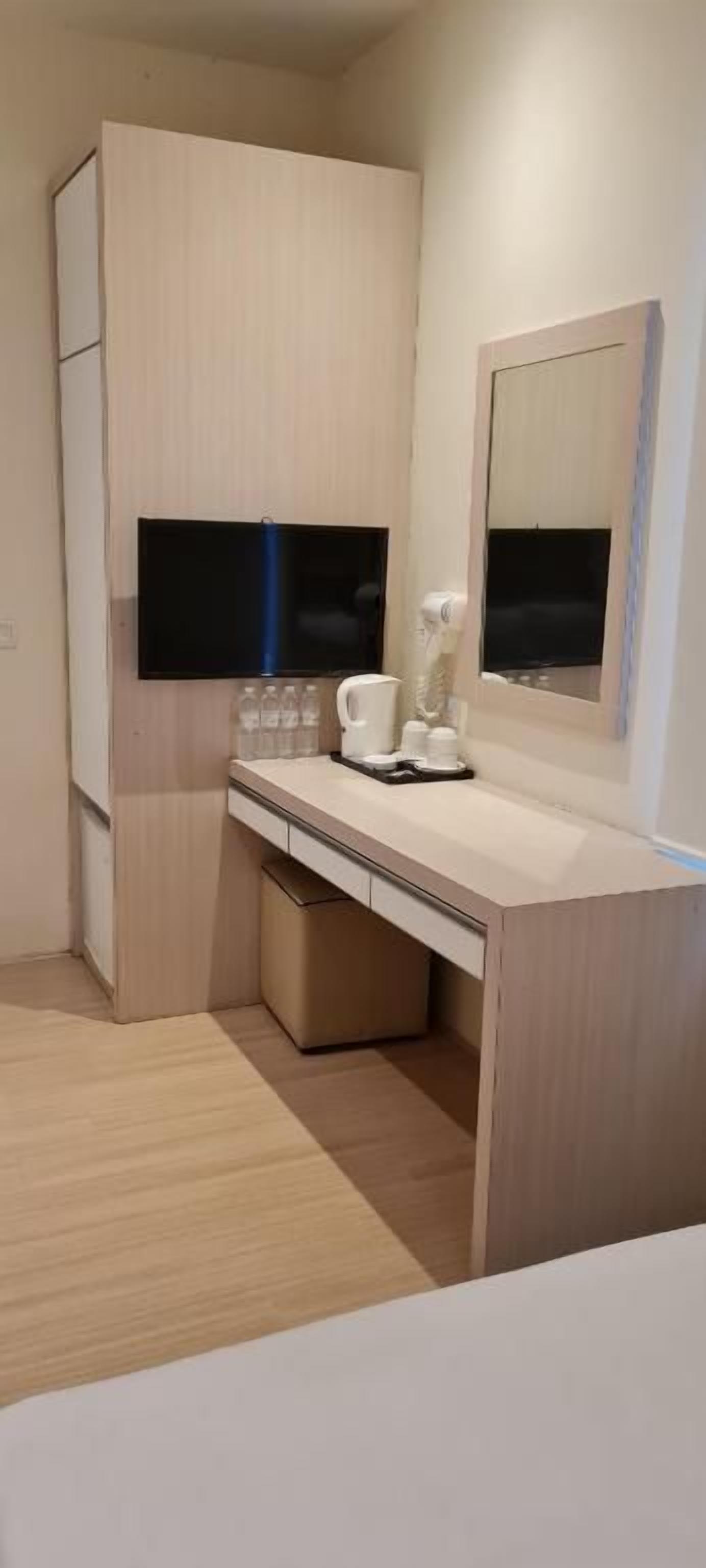 A compact hotel room with a kitchenette, a bed, a bedside table, a mirror, and a television.