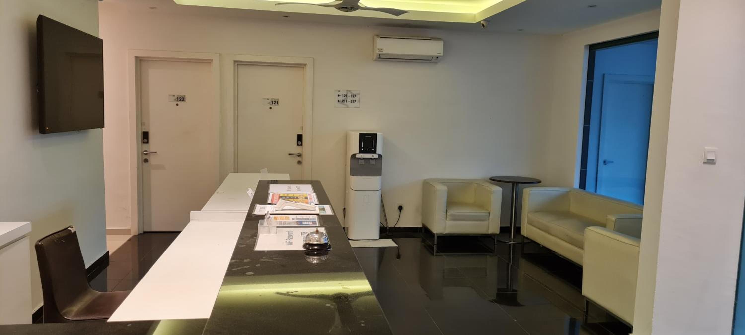 A hotel room with a long table, a sofa, a small round table, and a water dispenser.