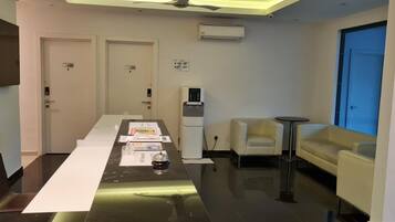 A hotel room with a long table, a sofa, a small round table, and a water dispenser.