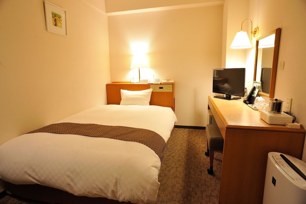 Ein Hotelzimmer mit Bett, Schreibtisch, Computer, Lampe und Spiegel.